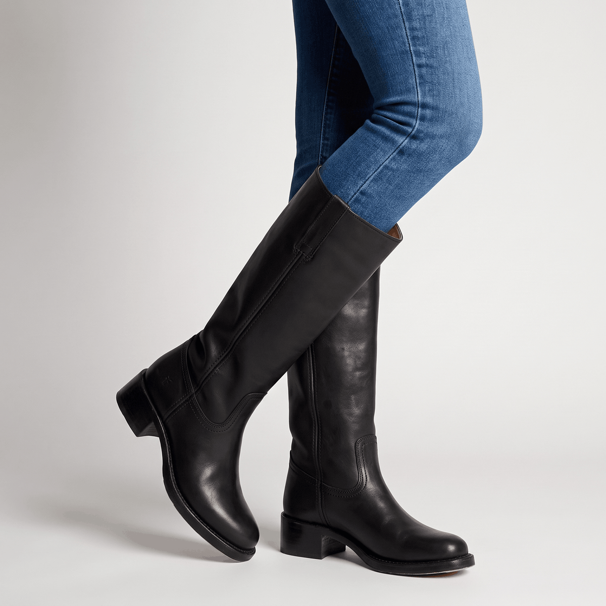 Woman wearing dark brown vegan leather knee-high boots with blue jeans.