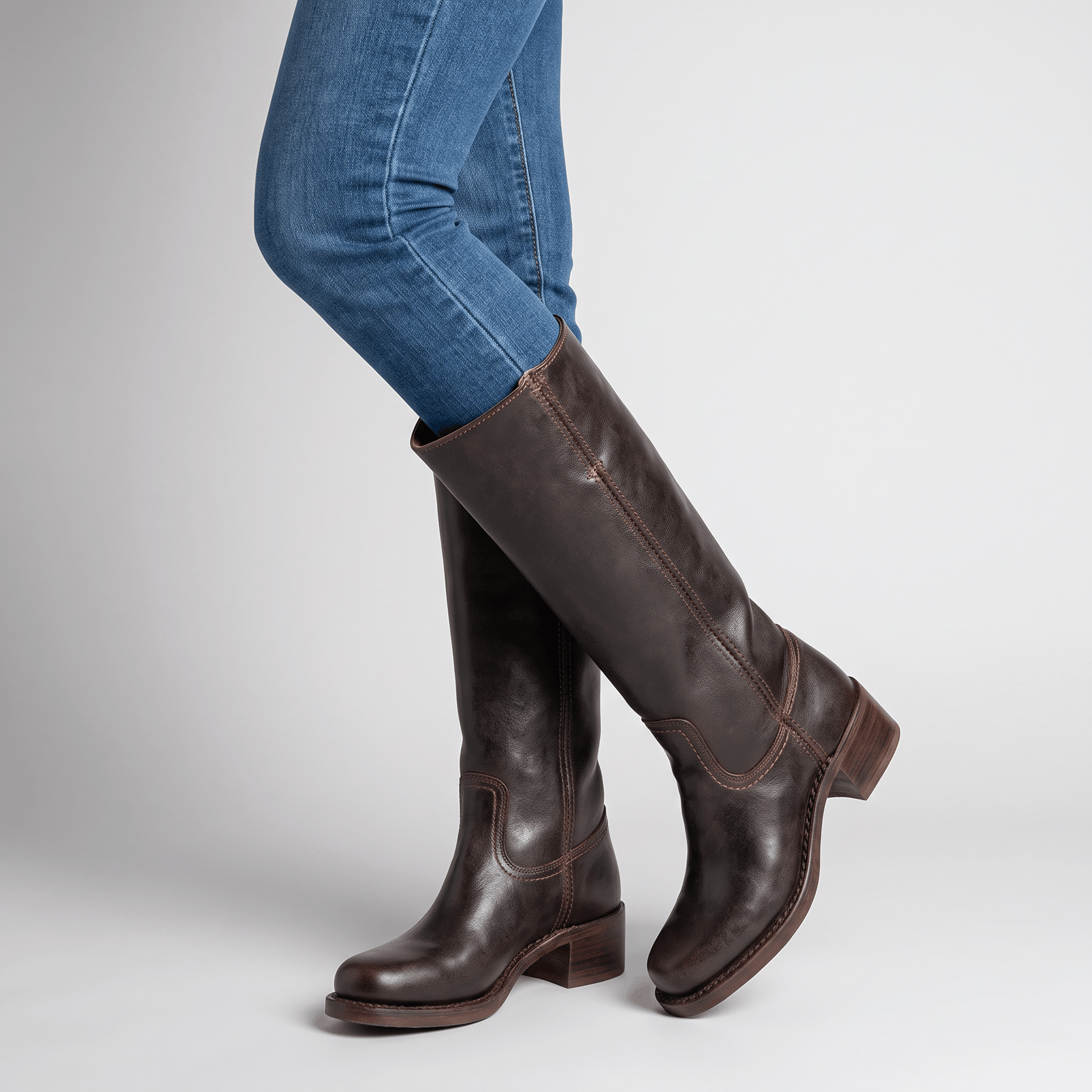 Close-up of dark brown vegan leather knee-high boots with block heels worn by a seated woman.