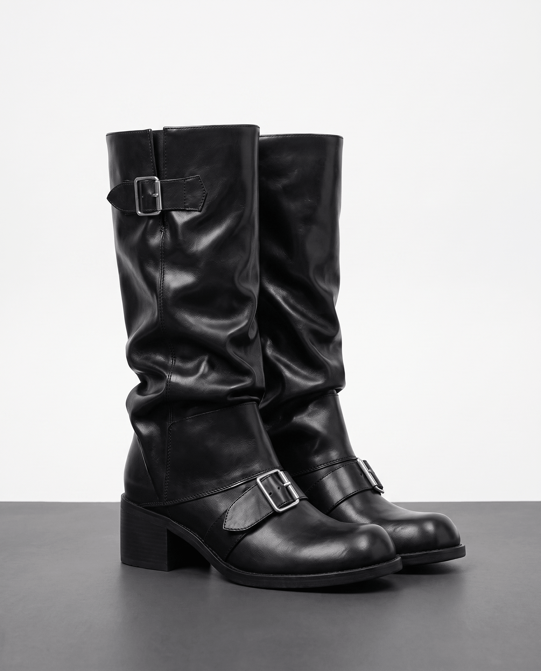 Black vegan leather mid-calf boots with ruched slouch shafts, dual buckle straps, and stacked block heels.