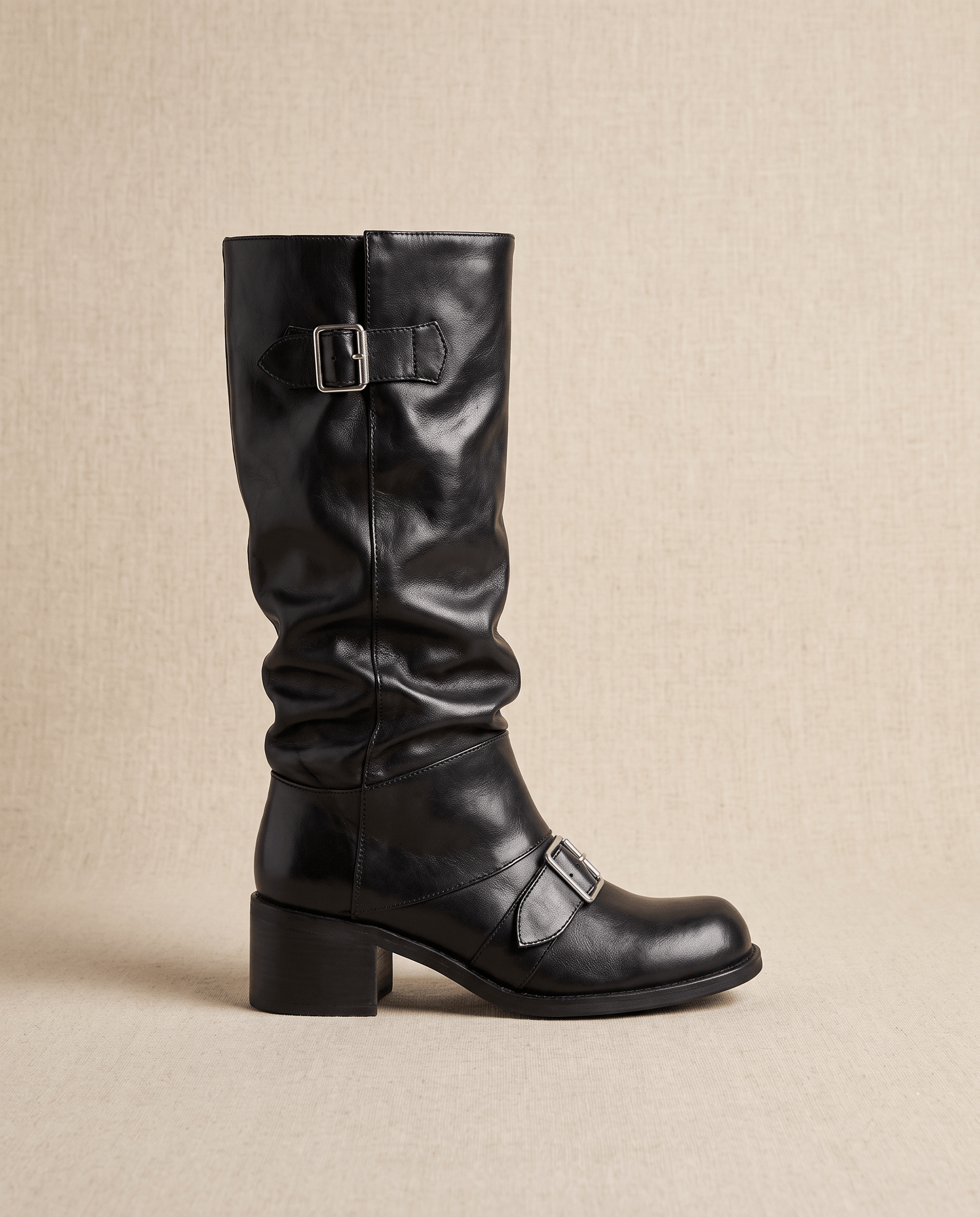 Black vegan leather mid-calf boots with a ruched slouch shaft, double buckle straps, and a stacked block heel.