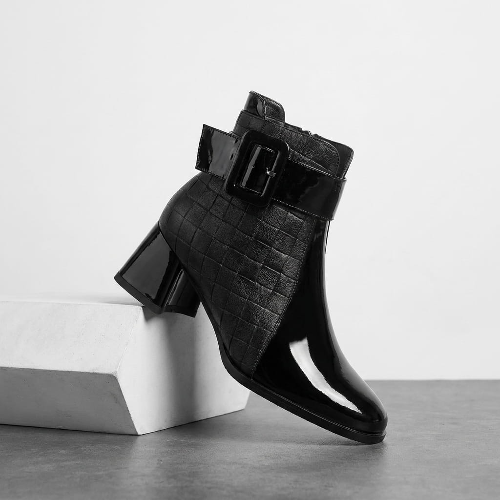 Black square-toe vegan leather ankle boot with a block heel, displayed on a white pedestal.