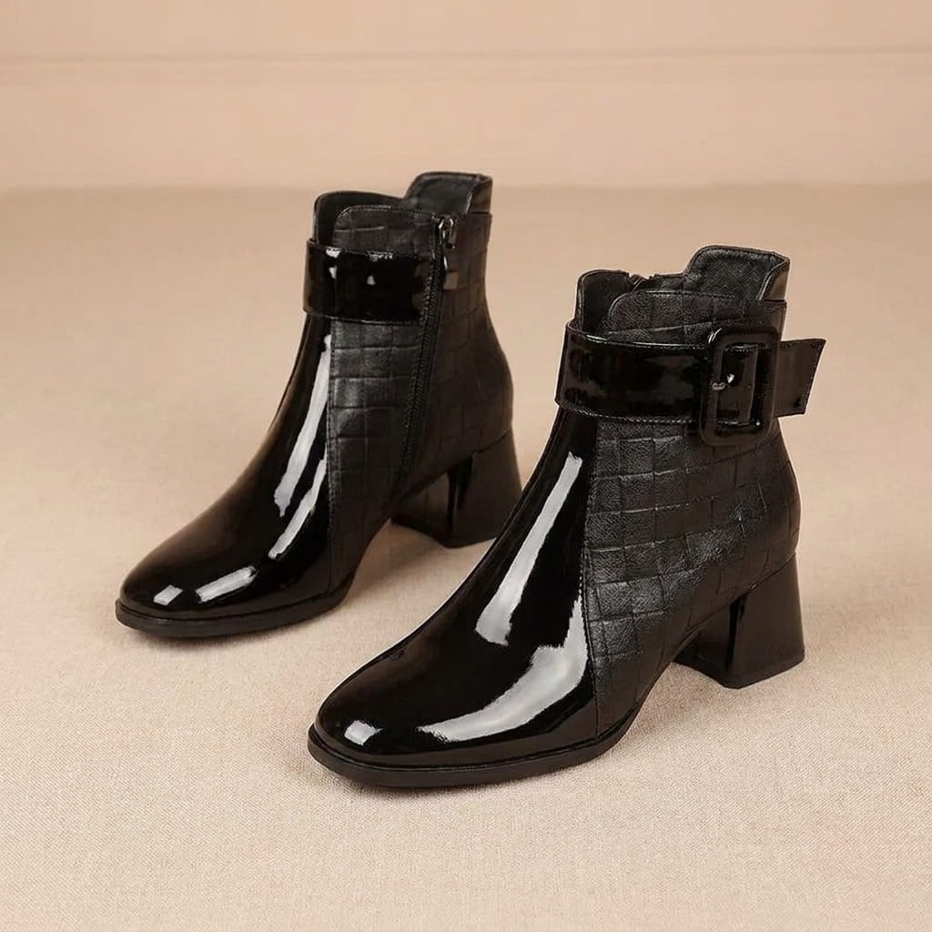 Pair of black and brown croc-embossed vegan leather ankle boots on a beige background.