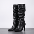 Black vegan leather knee-high boots with a ruched slouch shaft, pointed toe, and slim stiletto heel.