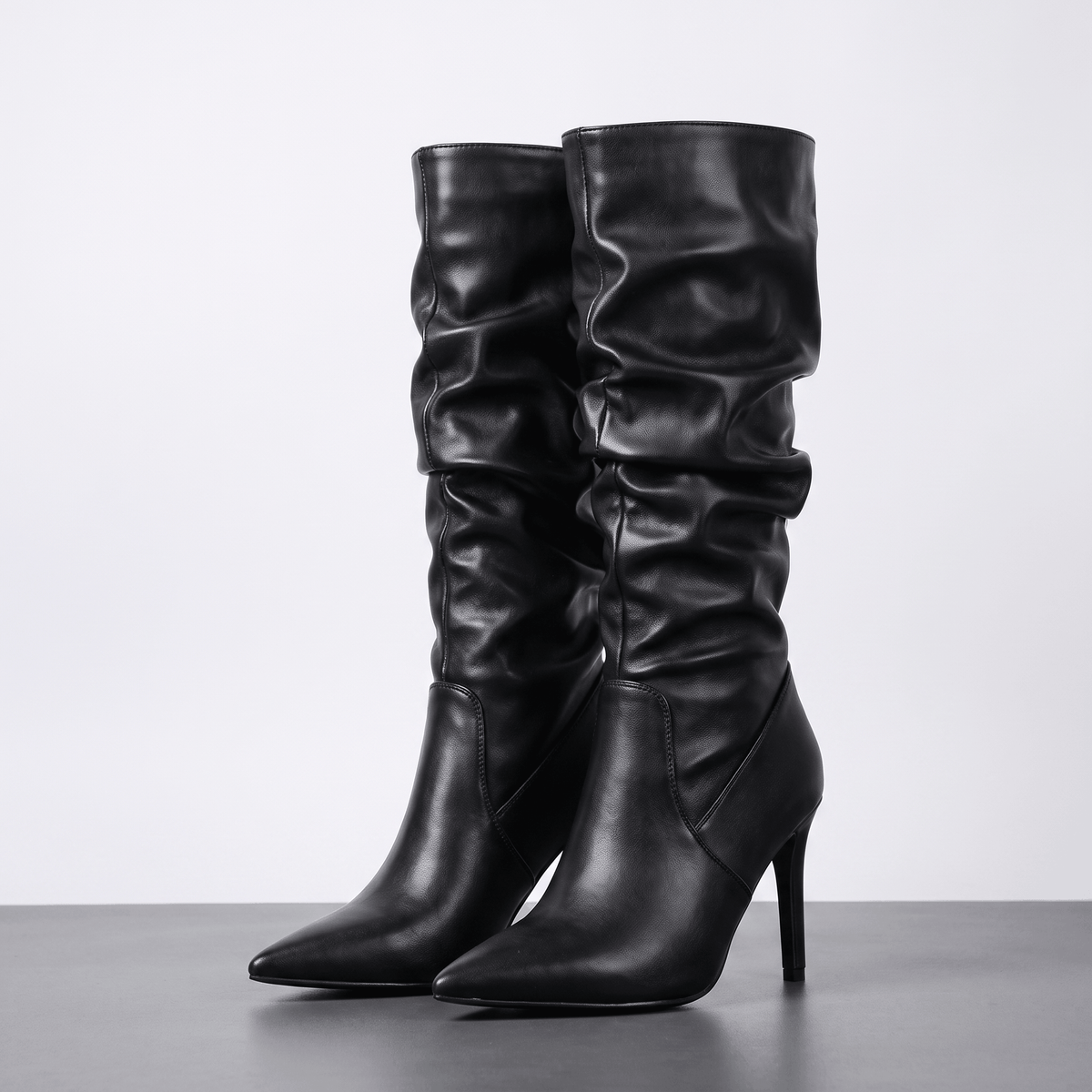 Black vegan leather knee-high boots with a ruched slouch shaft, pointed toe, and slim stiletto heel.