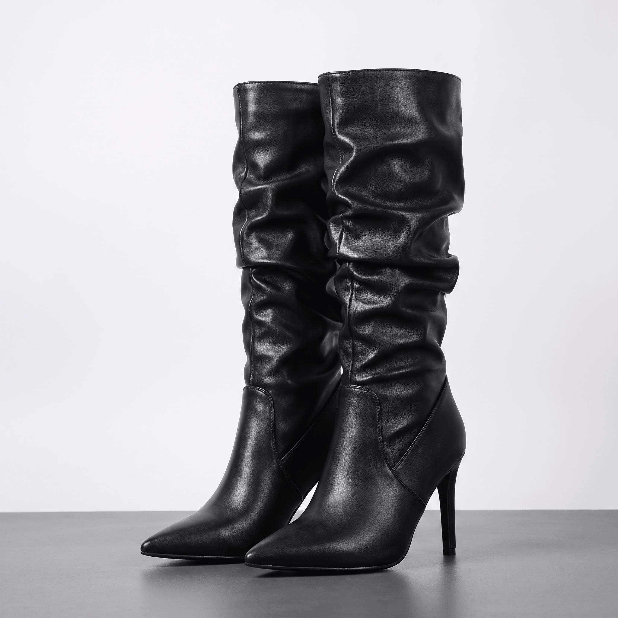 Black vegan leather knee-high boots with a ruched slouch shaft, pointed toe, and slim stiletto heel.