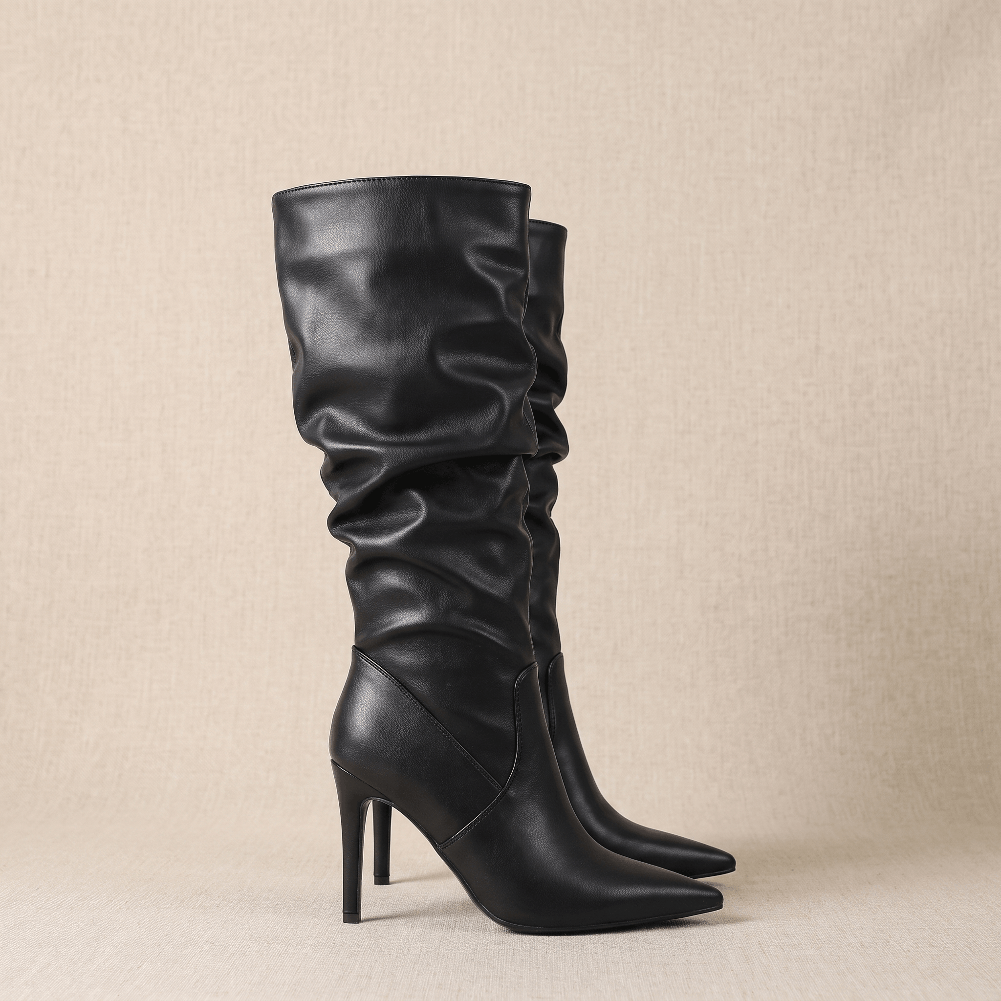 Black vegan leather stiletto knee-high boots with a ruched slouch shaft and a sharp pointed toe.