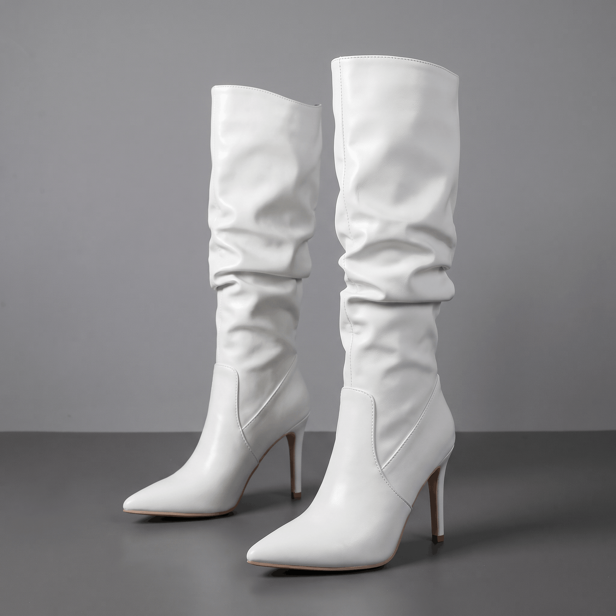 White vegan leather knee-high boots with a ruched slouch shaft, pointed toe, and slim stiletto heel.