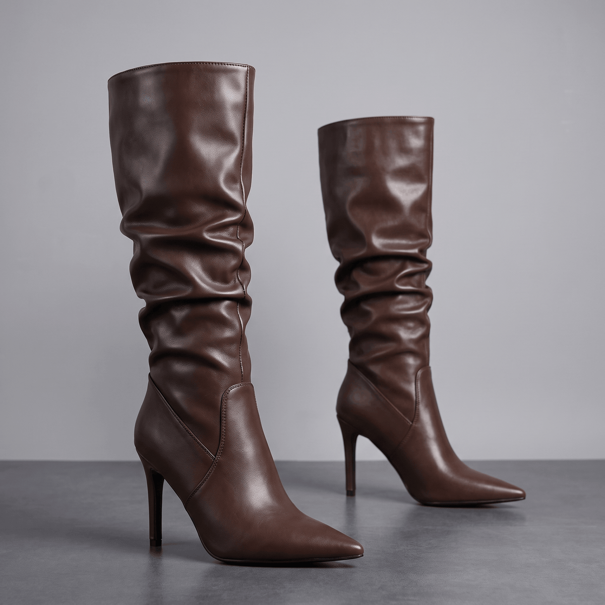 Brown vegan leather knee-high boots with a ruched slouch shaft, pointed toe, and slim stiletto heel.