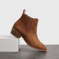 Brown vegan suede Chelsea boots with a block heel displayed on a white pedestal.