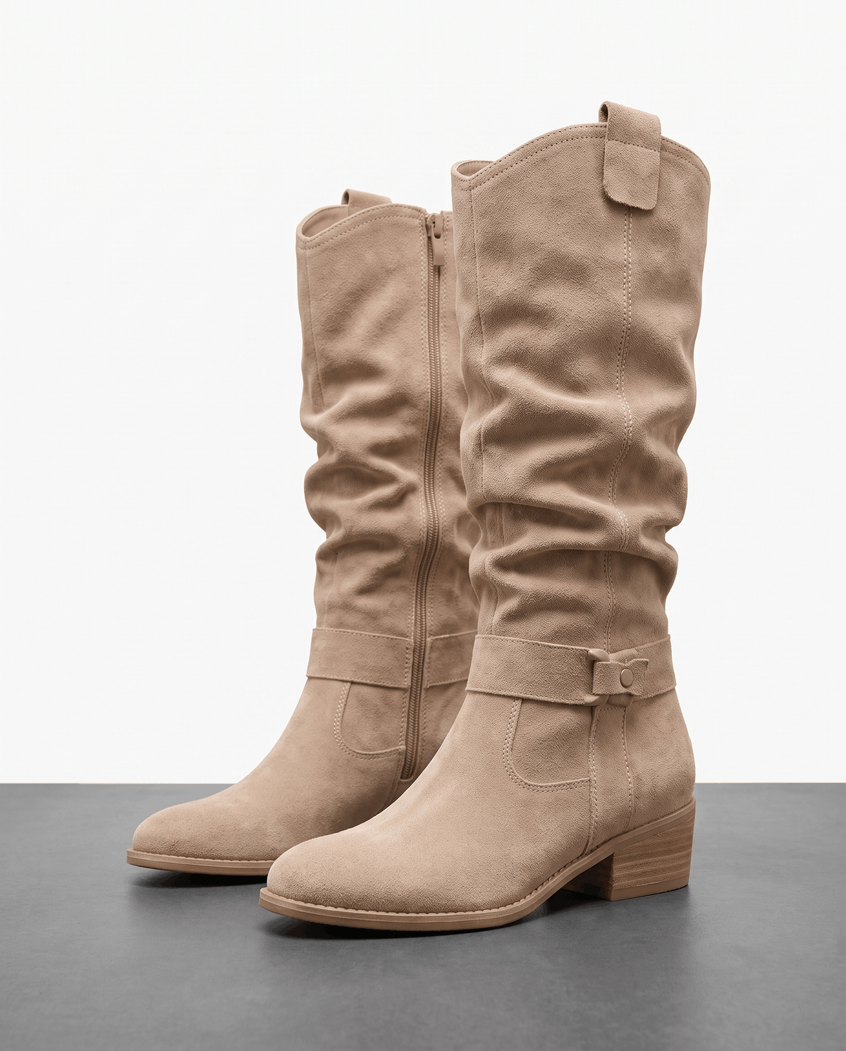 Pair of beige vegan suede knee-high slouch boots with a full side zip, ankle strap, and low stacked heel.