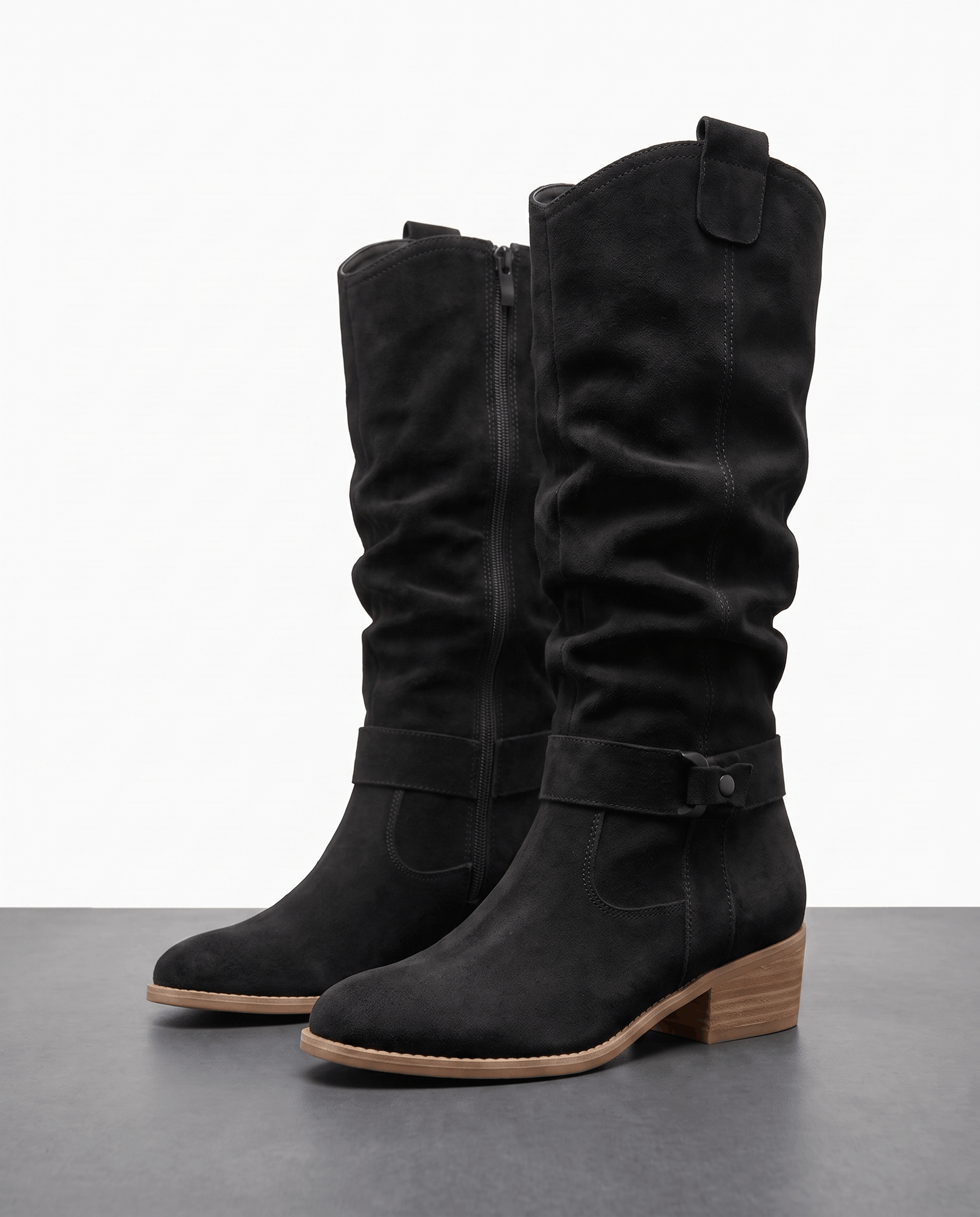 Pair of black vegan suede knee-high slouch boots with a full side zip, ankle strap, and low stacked heel.