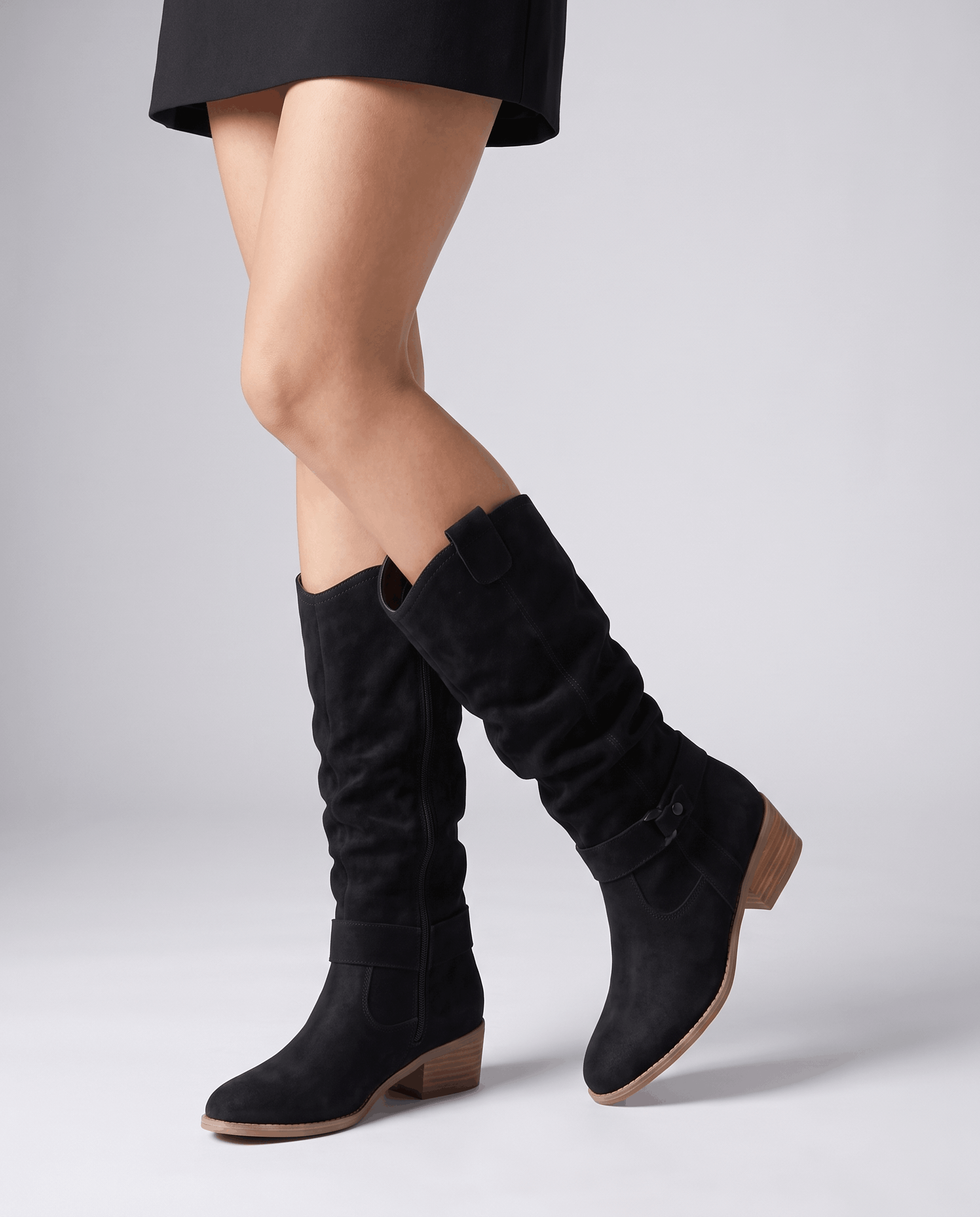 Woman walking in black vegan suede knee-high slouch boots with a black skirt.