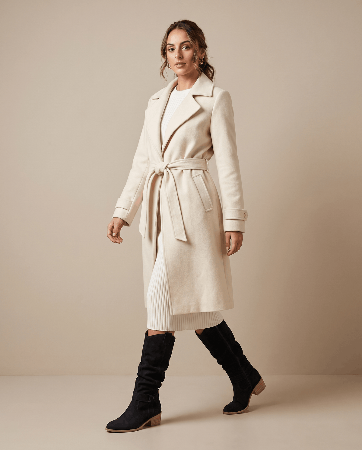 Woman wearing black vegan suede knee-high slouch boots with a cream belted coat.