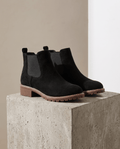 Black vegan suede Chelsea boots with elastic side panels, a stitched welt, and a chunky lug outsole on a concrete block.
