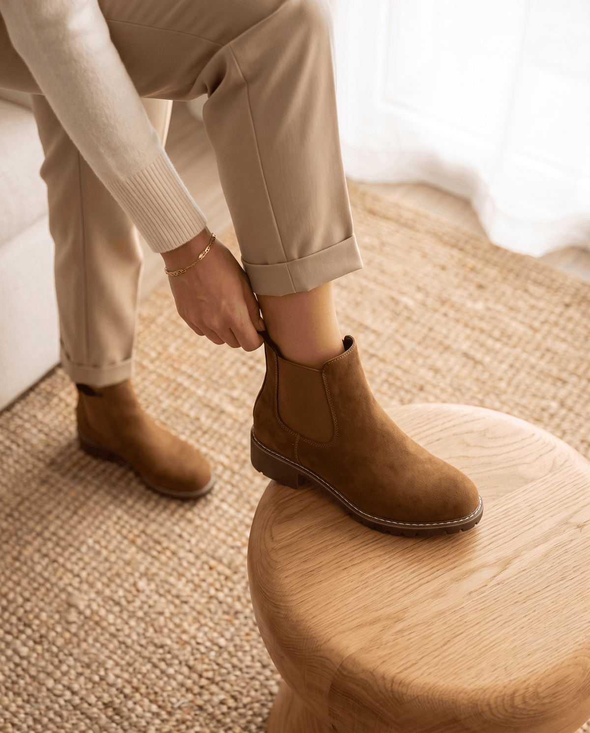 Brown vegan suede Chelsea boots with elastic side panels, a stitched welt, and a lug outsole worn with beige trousers.
