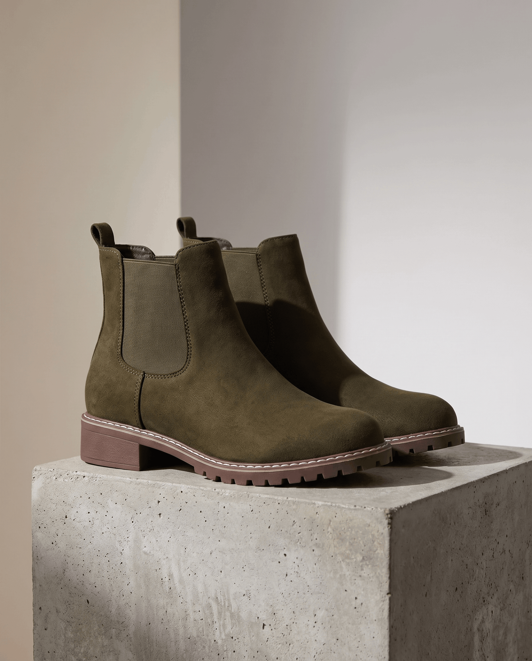 Green vegan suede Chelsea boots with elastic side panels, a stacked block heel, and a lug outsole on a concrete block.