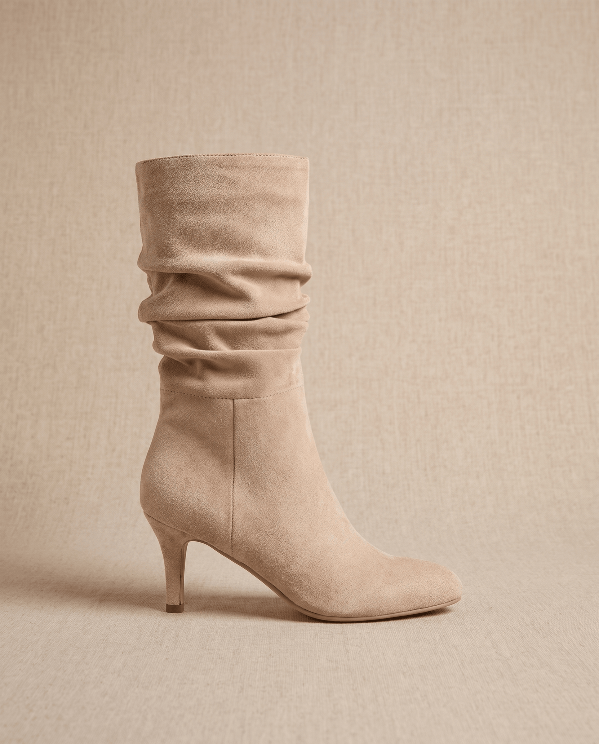 Light beige vegan suede mid-calf boots with a slouchy shaft, almond toe, and slim flared heel on a textured background.