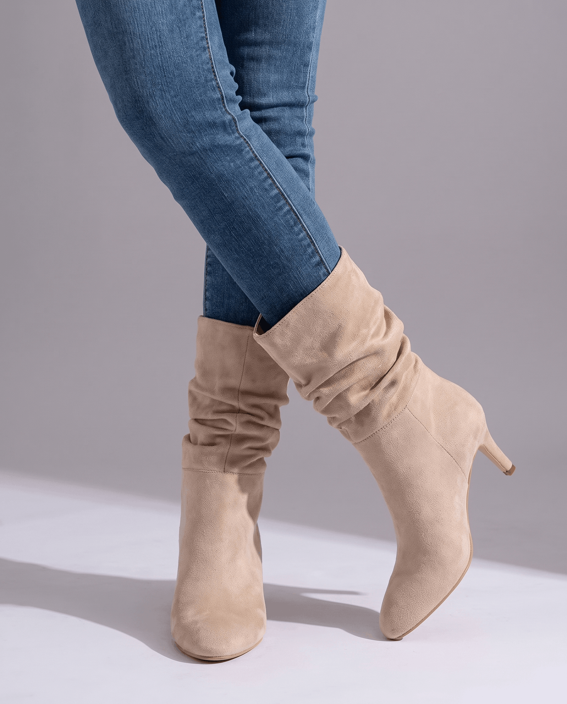 Light beige vegan suede mid-calf boots with a slouched shaft, almond toe, and slim flared heel worn over blue denim jeans.