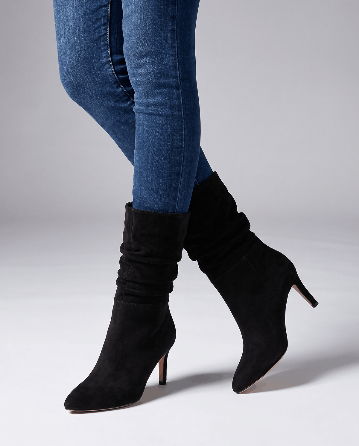 Black vegan suede mid-calf boots with a slouched shaft, almond toe, and slim flared heel worn over blue denim jeans.