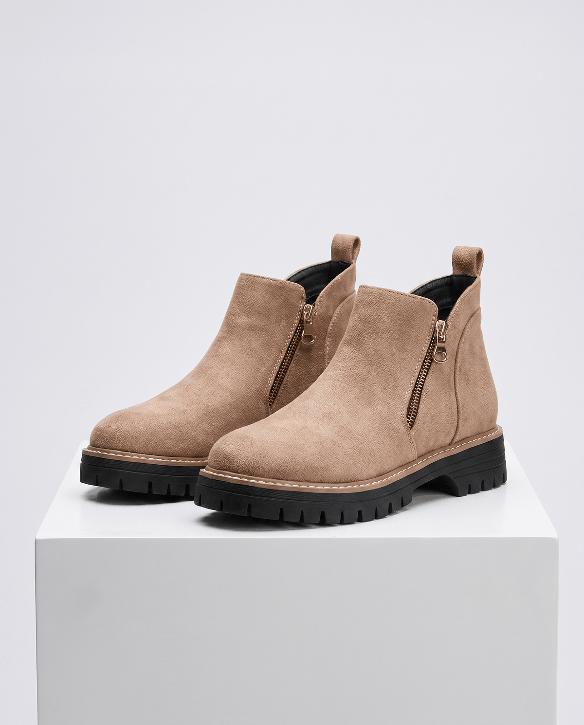 Taupe vegan suede ankle boots with side zips, chunky black lug platform soles, and cushioned wedge heels on a white pedestal.