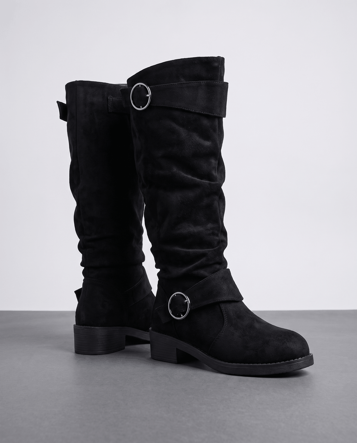 Black vegan suede knee-high boots with a slouched shaft, round toe, low stacked heel, and twin silver ring straps.