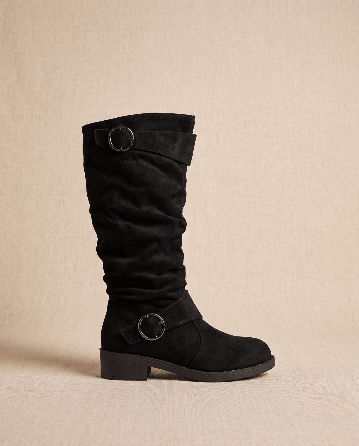 Black vegan suede knee-high boot with a slouched shaft, round toe, low stacked heel, and twin decorative ring straps.