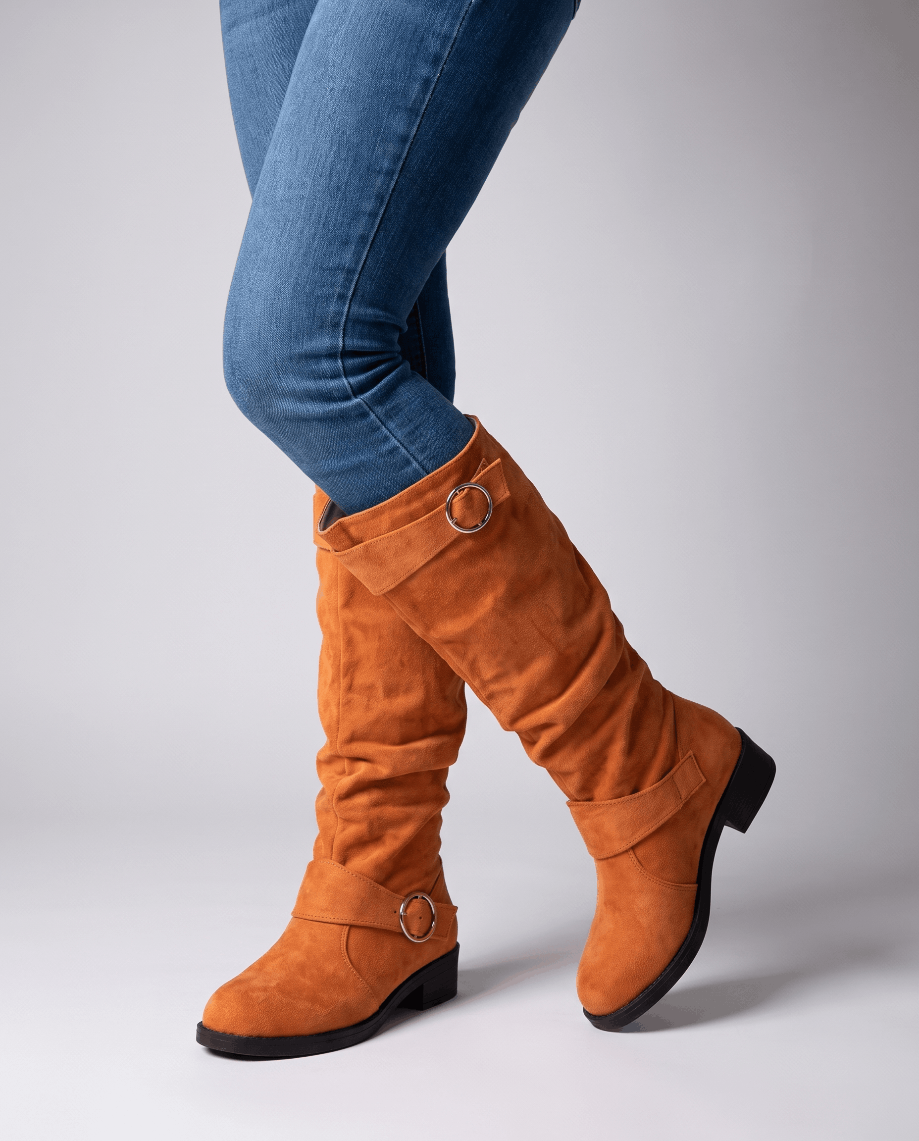 Orange vegan suede knee-high boots with a slouched shaft, twin ring straps, round toe, and a low heel worn over blue jeans.