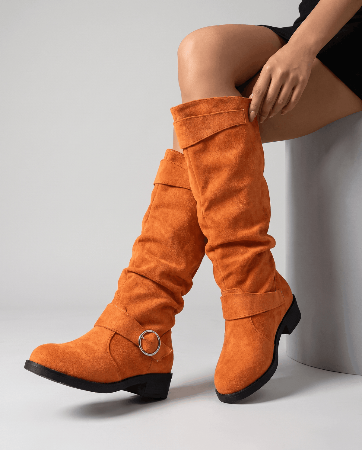 Orange vegan suede knee-high boots with a slouched shaft, twin ring straps, and a low stacked heel on a round toe.