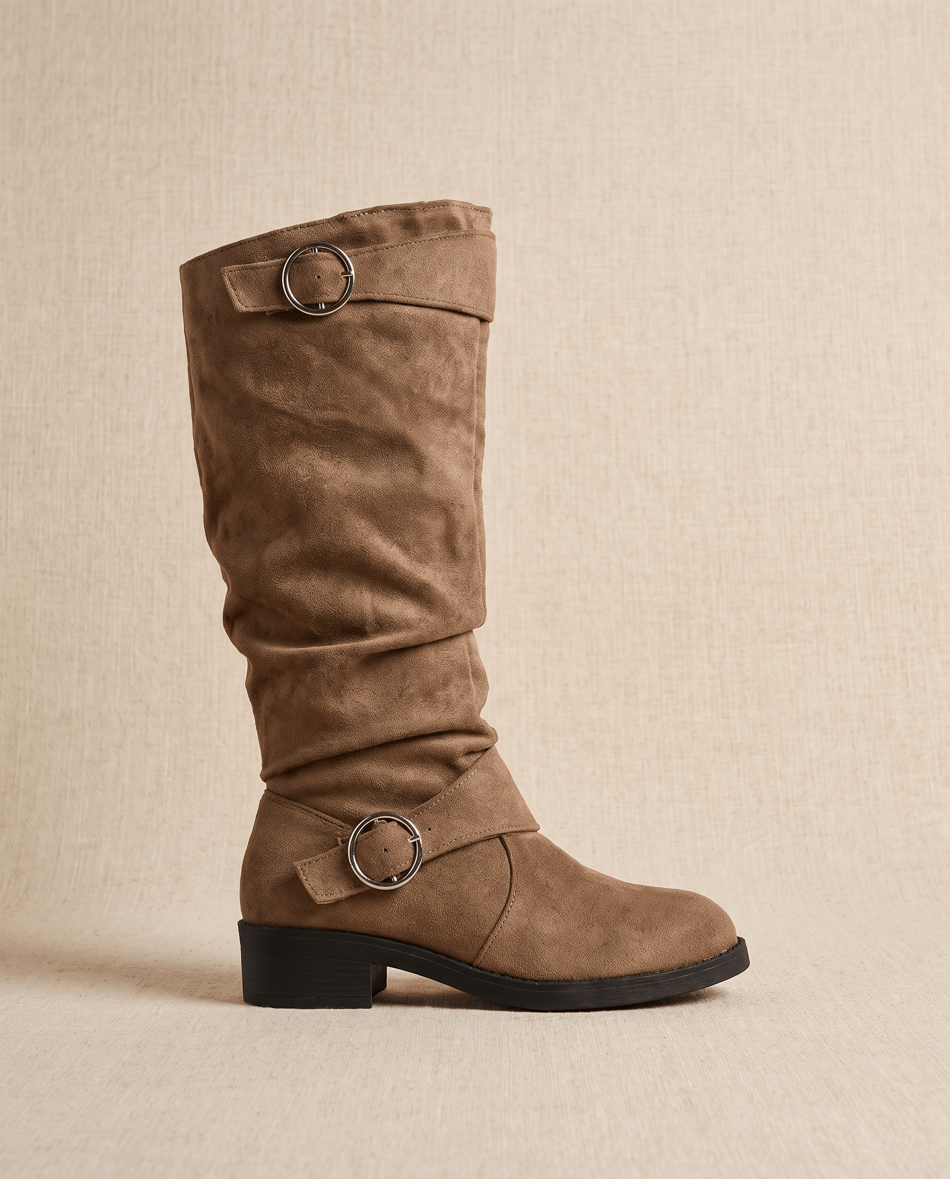 Brown vegan suede knee-high boots with a slouched shaft, round toe, low stacked heel, and twin decorative ring straps.