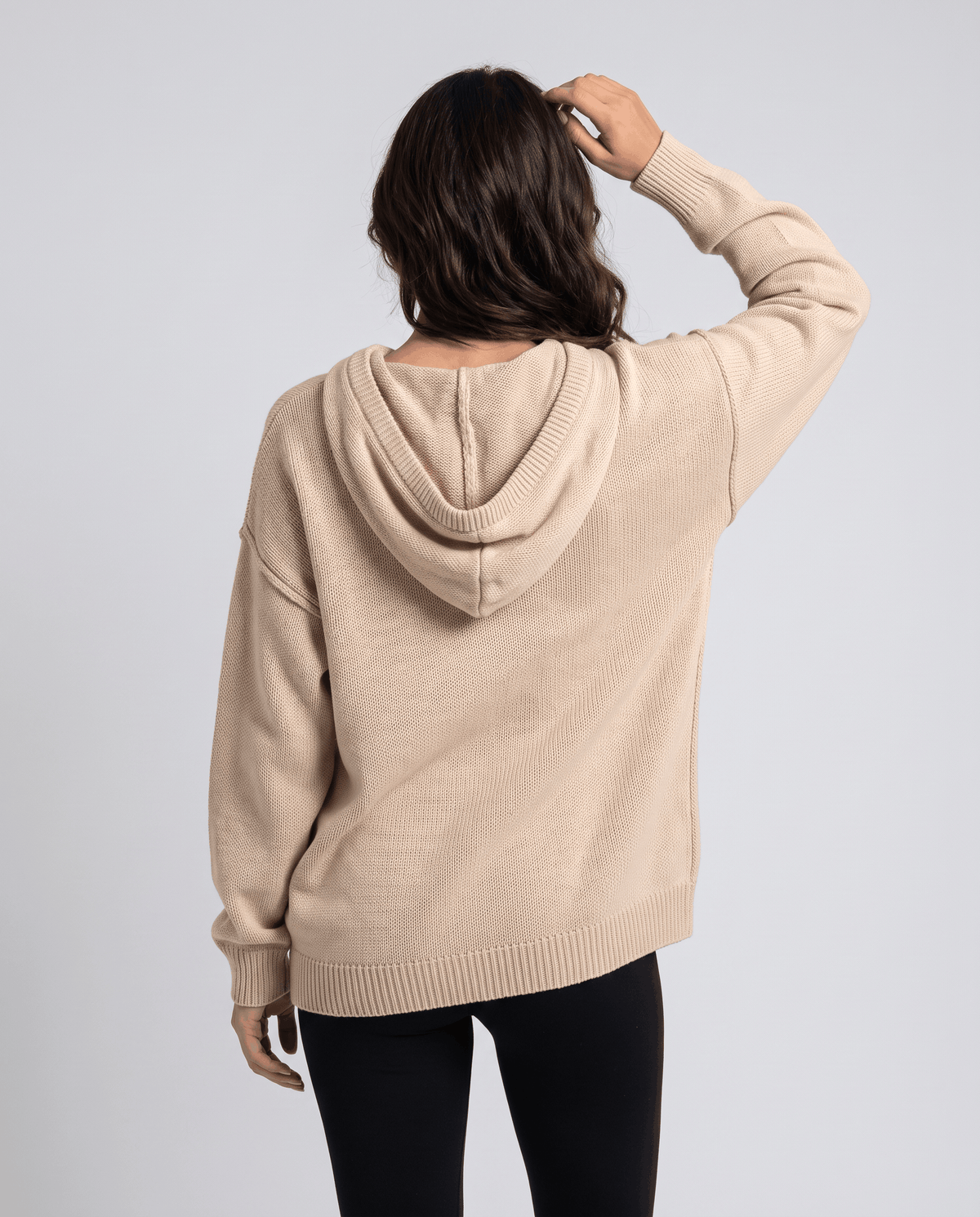 Back view of the beige knit hoodie with the hood down and black pants