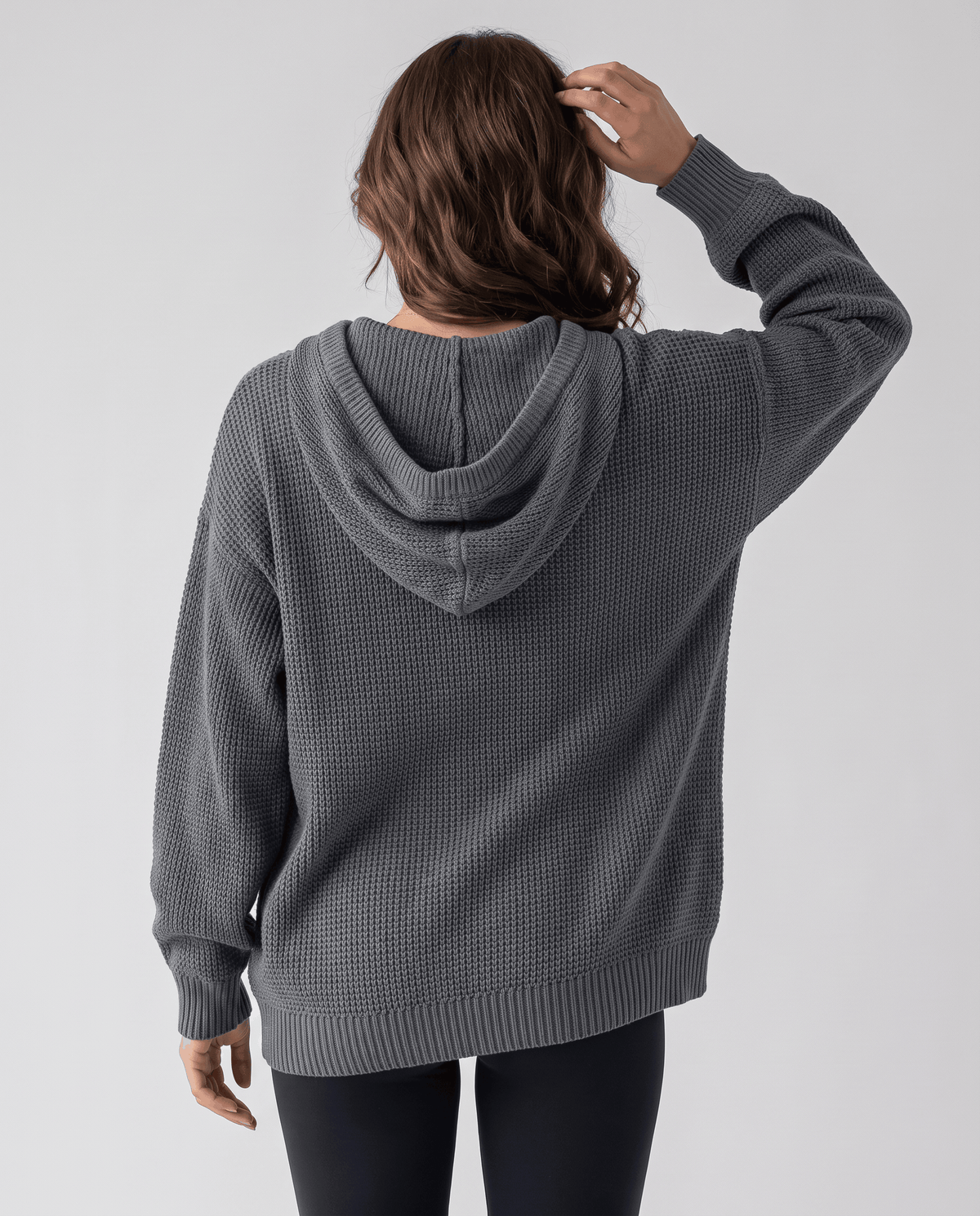Back view of the gray waffle knit hoodie with the hood down and hands at the head