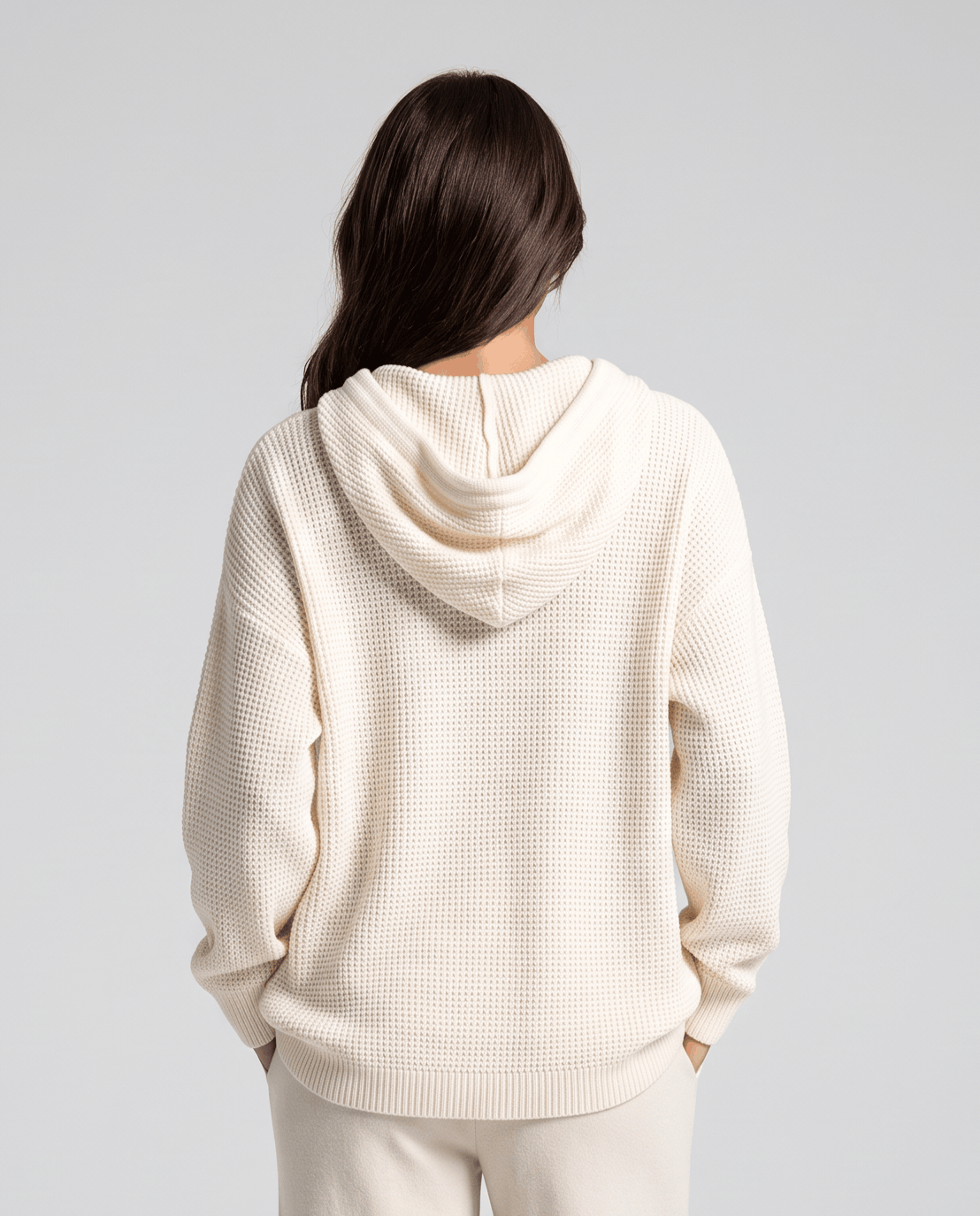 Back view of the white waffle knit hoodie with the hood down over cream pants