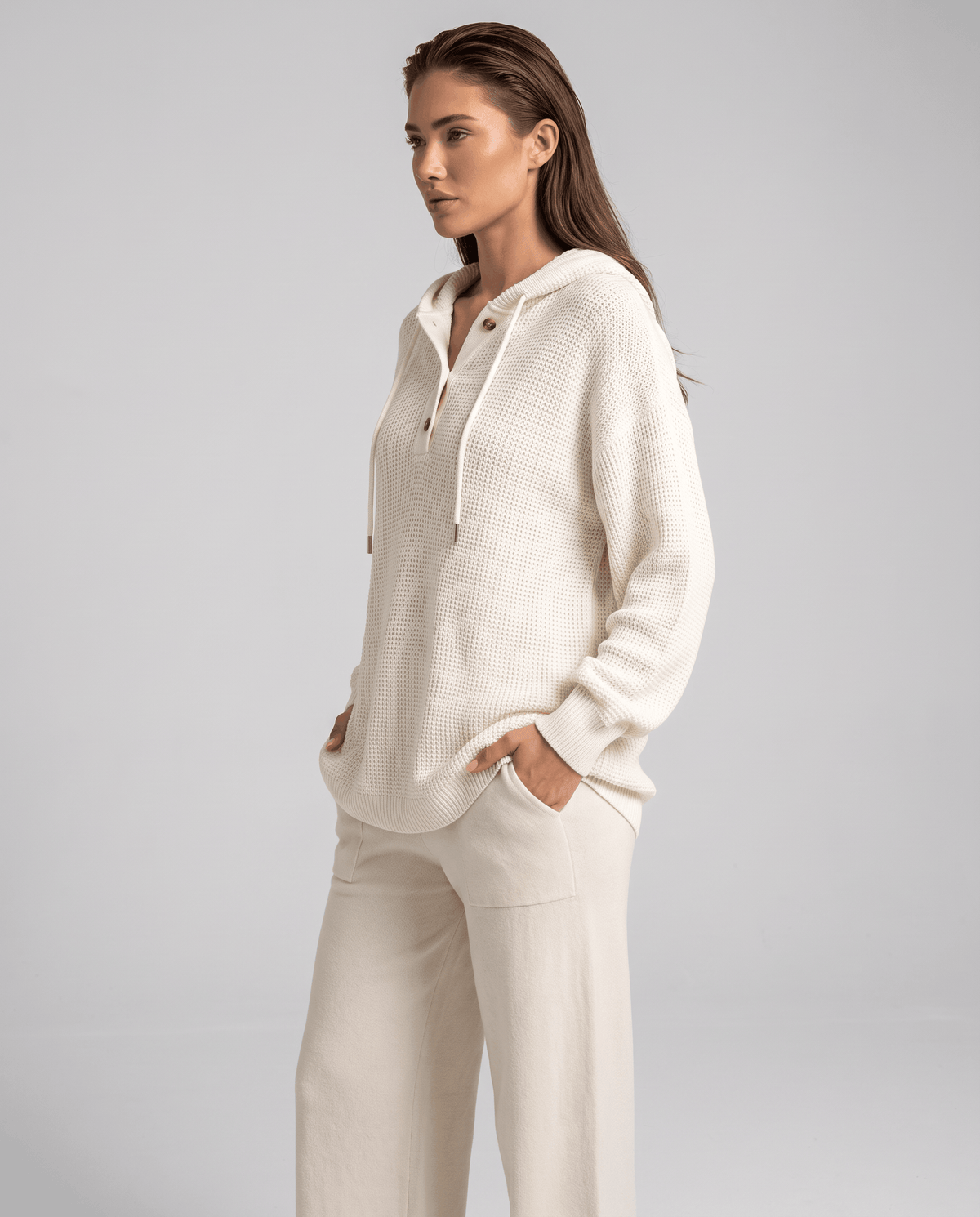 Full-length look pairing the white knit hoodie with cream wide-leg pants, hands in pockets