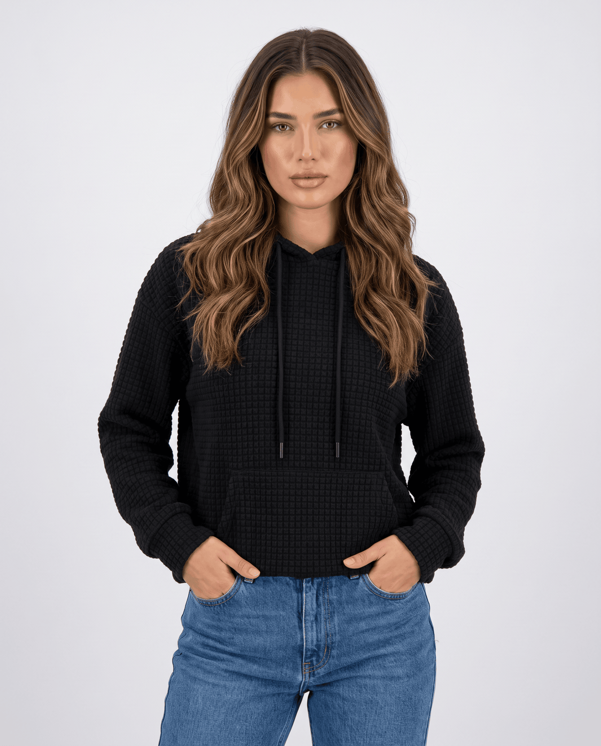 Front view of black waffle knit hoodie worn with jeans and hands in the pocket