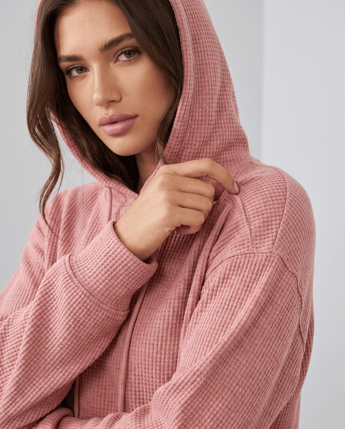 Close-up of dusty pink waffle knit hood with a hand on the drawstring and ribbed cuff