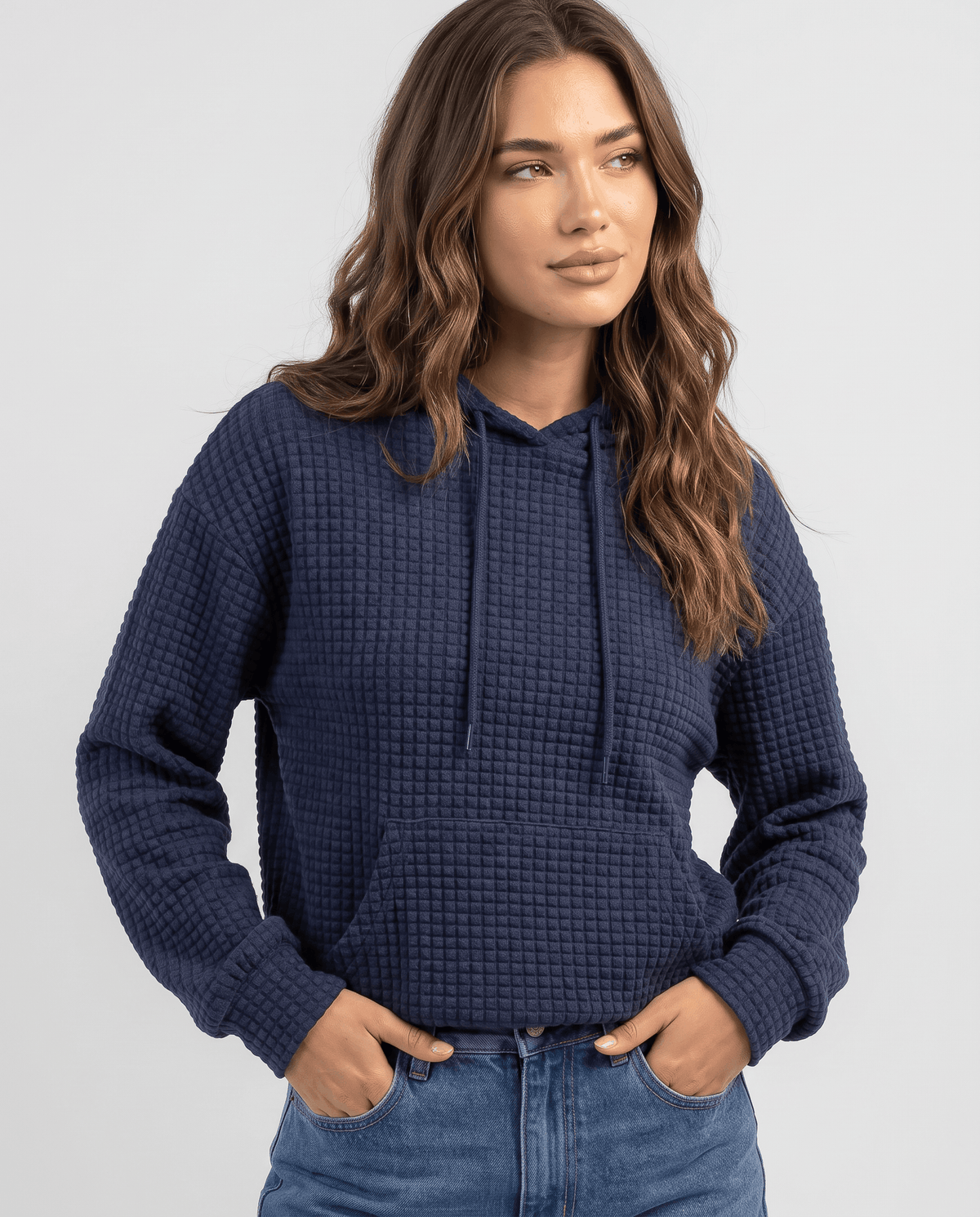Front view of navy blue waffle knit hoodie with drawstrings and hands in jeans pockets