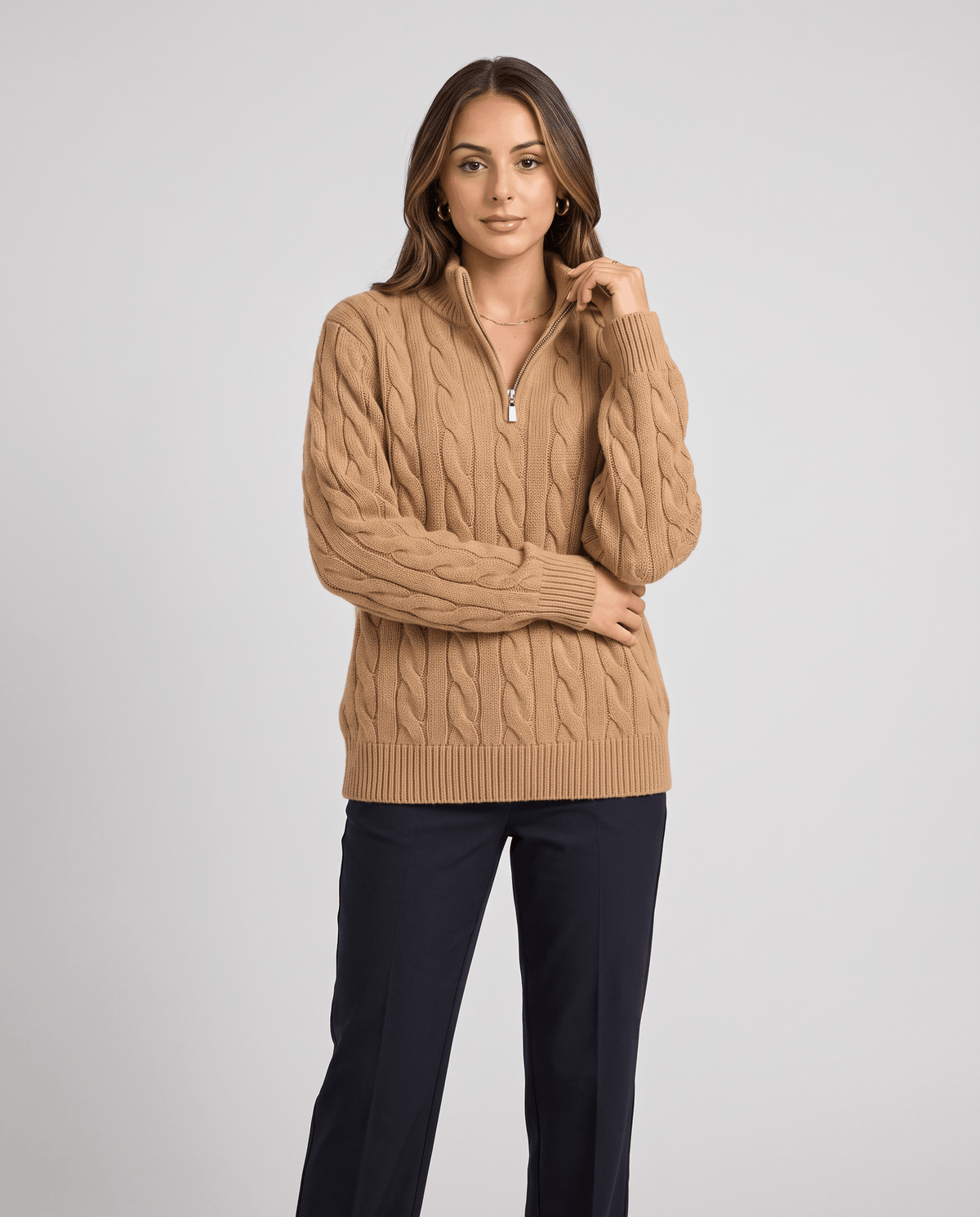 Model touching the stand collar of a camel sweater with navy trousers