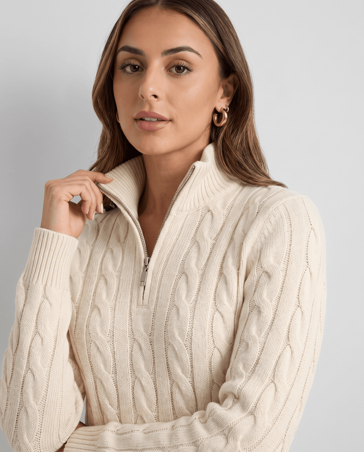 Model holding the half zip of a cream cable-knit sweater