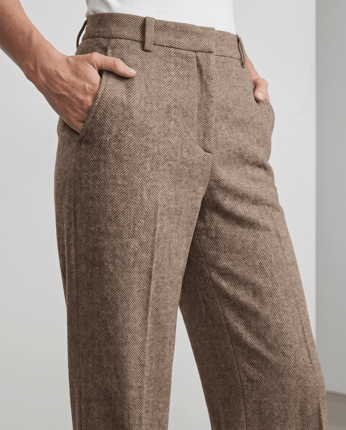 Close-up of camel herringbone trousers with belt loops and pressed front crease