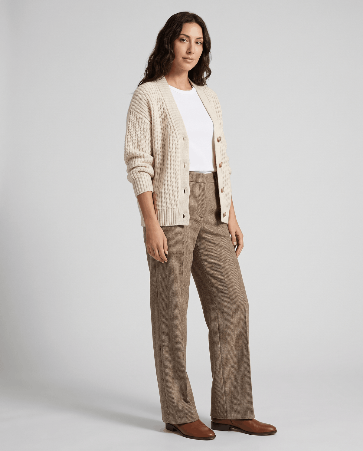 Model in cream cardigan and white tee wearing camel herringbone trousers