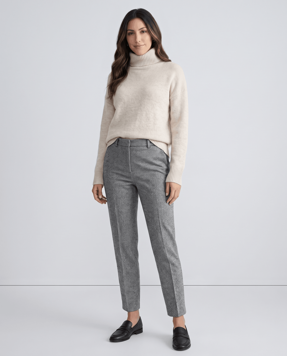 Model in cream turtleneck sweater and gray herringbone trousers with loafers