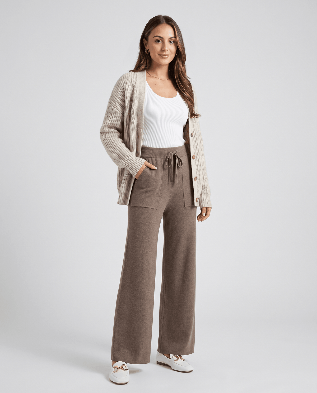 Model in oatmeal cardigan and white tank wearing beige knit pants