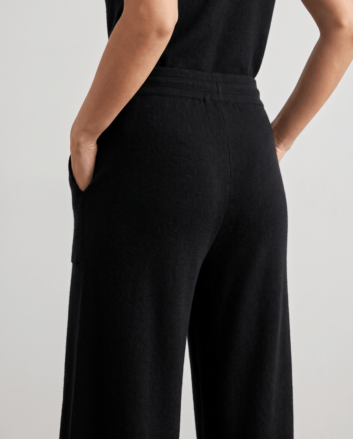 Back detail of black high-waisted knit pants with hand in pocket