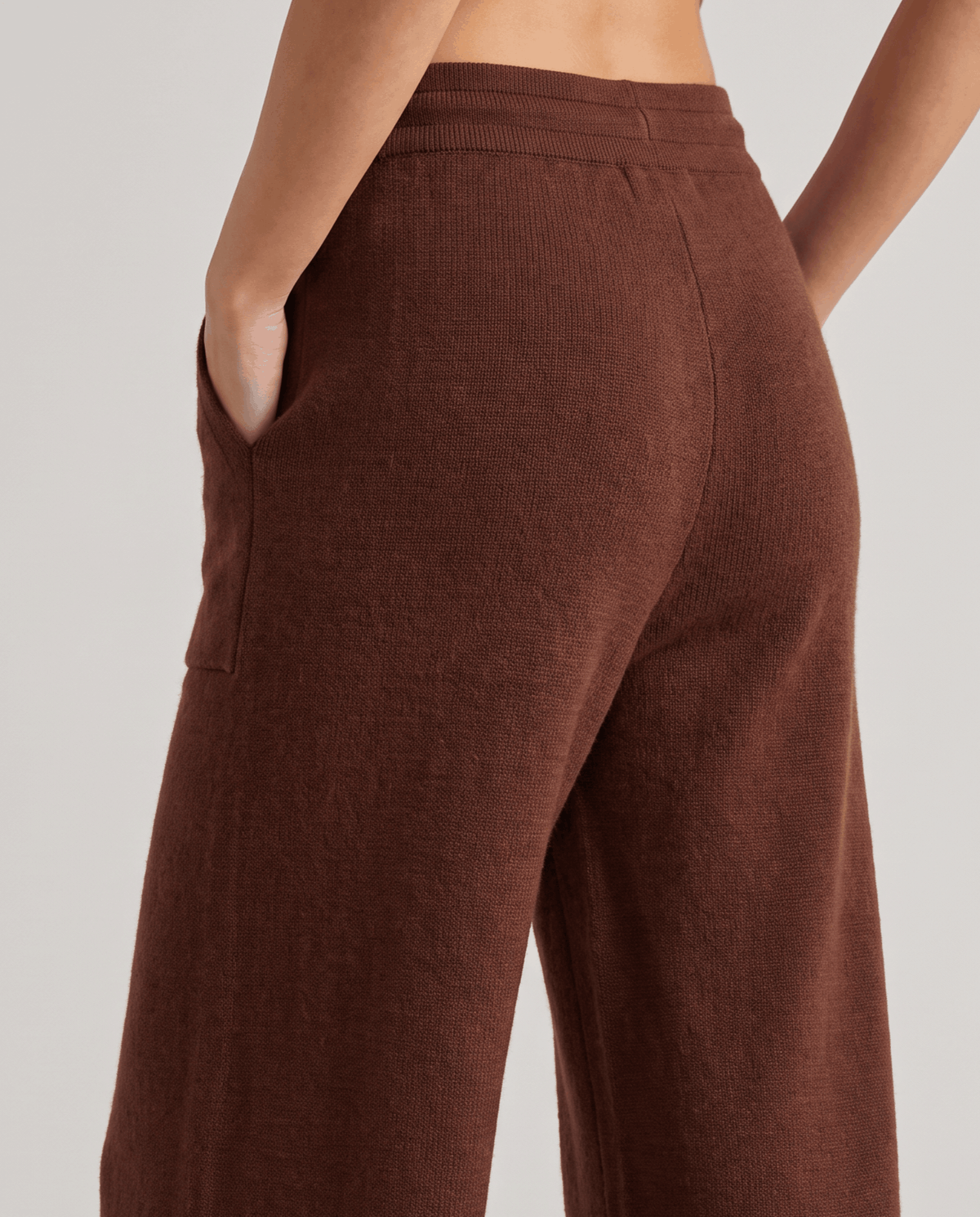Back detail of brown knit pants with hand tucked in side pocket
